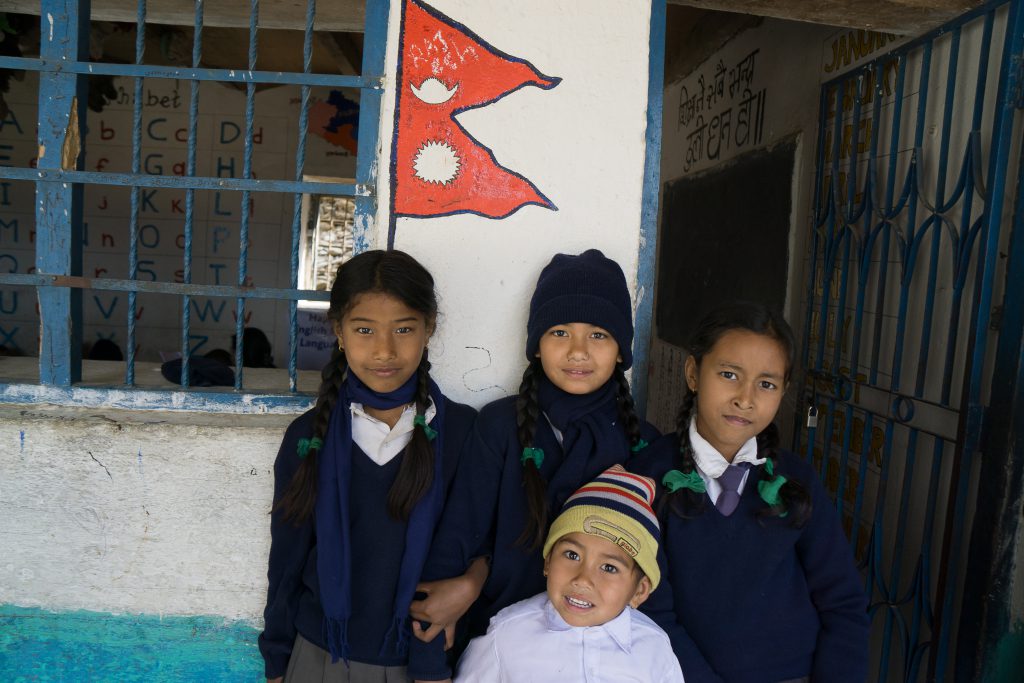 Quattro alunni della scuola di Uttargaya, in Nepal, davanti al fronte restaurato delle aule del blocco C